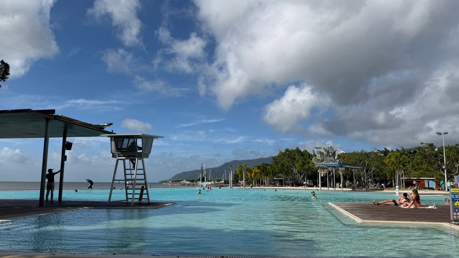 The Cairns Esplanade Lagoon with swimmers, a lifeguard tower and mountains in the distance